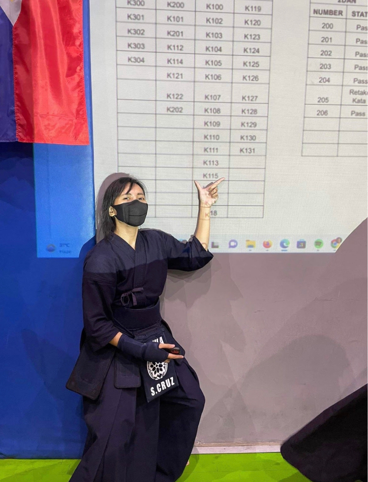 Sam pointing at her number, K115, in the list of kendoka who passed the exam